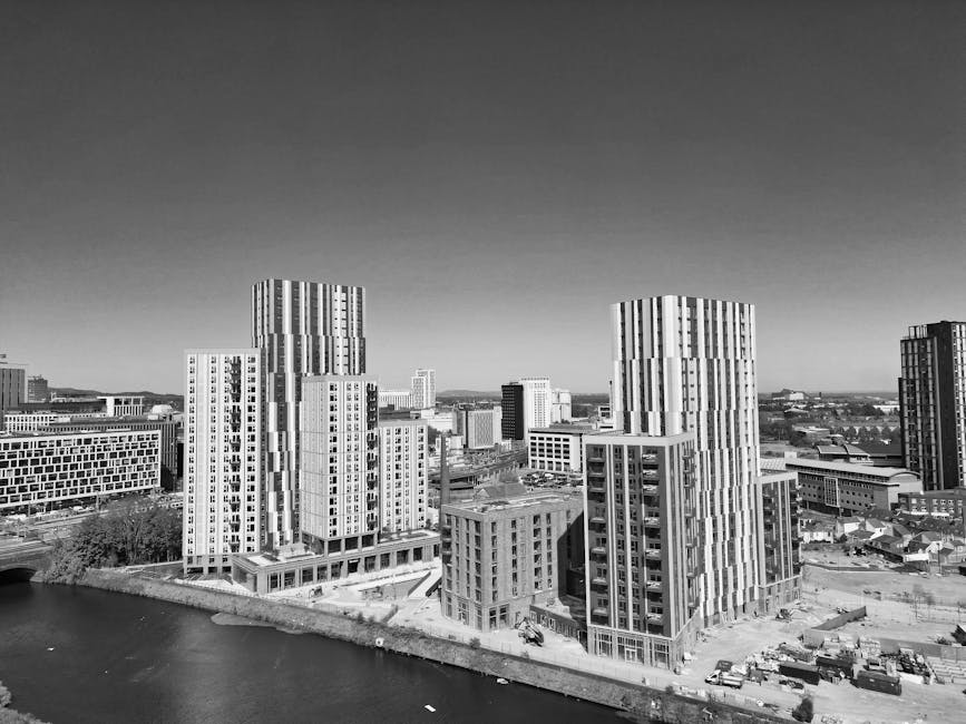 A black-and-white aerial view of a residential neighbourhood featuring rows of terraced houses, semi-detached homes, and small apartment buildings, with a clear sky overhead. The image captures a wide